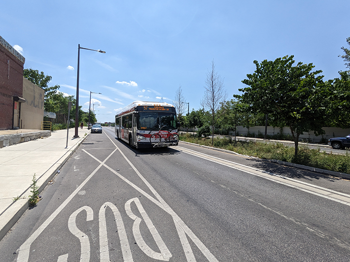 Bus moving down the street next to a green median with a tree