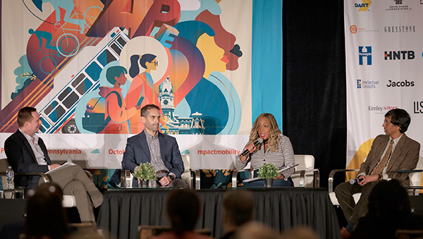 A group of 4 people seated on stage with a big colorful banner behind them.