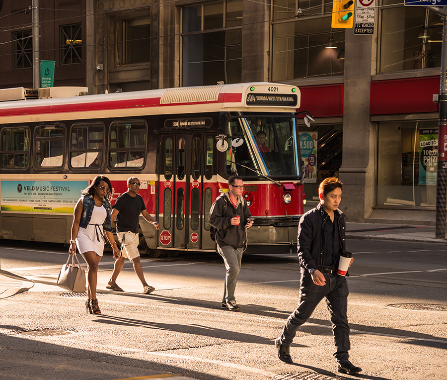 people crossing as red streetcar goes by in background